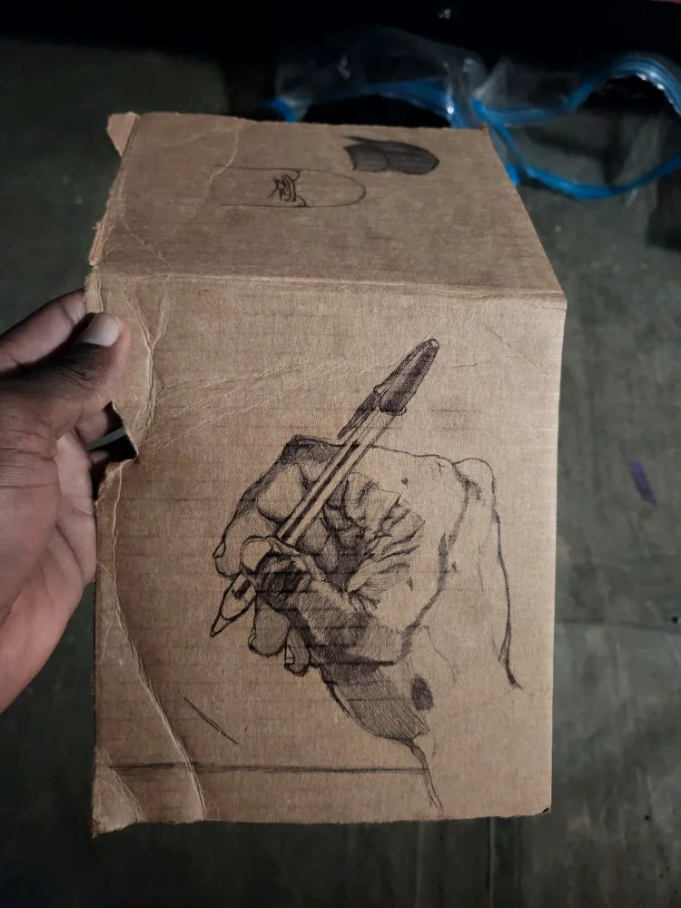 Percy holding a piece of cardboard with a detailed ballpoint pen drawing of a hand holding a pen.